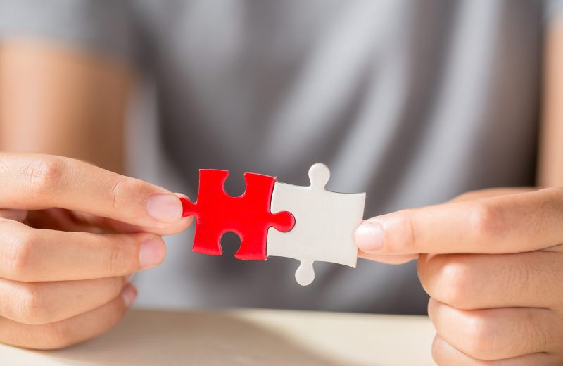 hand connecting two puzzle pieces on table background, business strategy concept